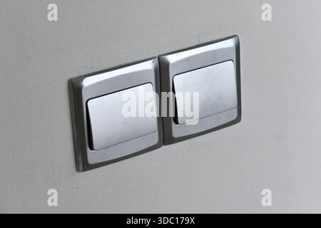 Close-up of two modern silver metal light switches installed side-by-side on a neutral-colored wall in a contemporary interior. Stock Photo