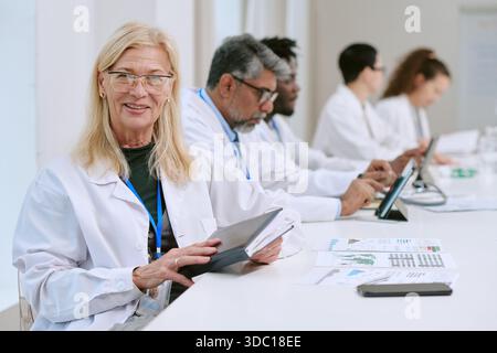 Senior Woman Scientist Using Tablet during Multiethnic Team Meeting Stock Photo
