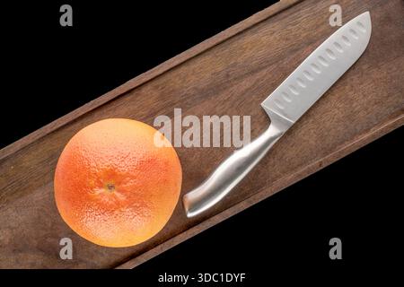 One juicy grapefruit with wooden kitchen board and knife on black background, close-up, top view. Stock Photo