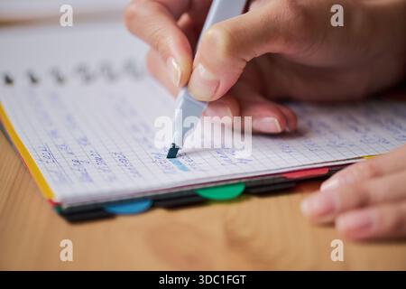 Woman using highlighter marker on squared notebook paper, closeup of right hand holding pen and making notes, visible fingernails and part of palm, wooden desk background Stock Photo