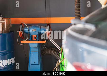 Rovigo, italy 18 december 2025: industrial bench grinder with orange support and blue base in a clean car repair workshop, close-up on metalworking to Stock Photo