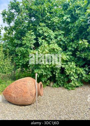 A rustic amphora pot sitting next to an old walking stick in a traditional green garden setting in the country of Georgia. Stock Photo