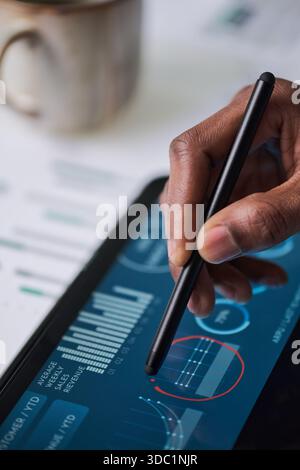 Black man using digital pen interacting with tablet displaying financial charts and analytics, hand holding stylus making notes on touchscreen, closeup of technology in business setting Stock Photo