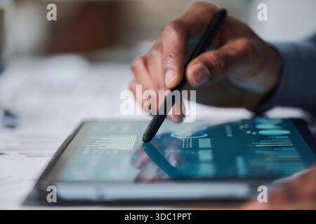 Black man using stylus interacting with digital tablet displaying data charts and graphs, close up of hand and device, focusing on technology usage in professional setting Stock Photo