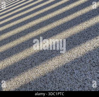 Geometric shadows casting parallel lines across a textured pebble surface Stock Photo