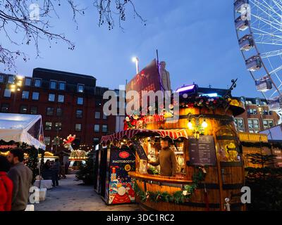 Manchester, UK - December 10, 2025: Festive market in Manchester featuring a wooden wine bar, bright decorations and a photobooth at dusk. Stock Photo