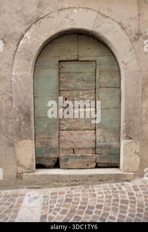 Old wooden door leading to a historic past, featuring worn textures and an arched stone frame set in an aged wall Stock Photo