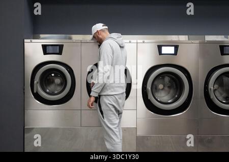 Man Using Self-Service Washing Machine in Modern Laundromat Stock Photo