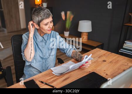 Focused mature businesswoman reviewing documents at home office desk Stock Photo