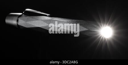Waterproof metal pocketlight flashlight with its LED shining on a black background. Stock Photo