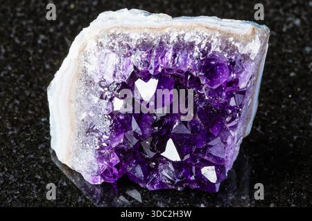 sample of rough geode of amethyst mineral crystals on black granite background close up from Russia Stock Photo