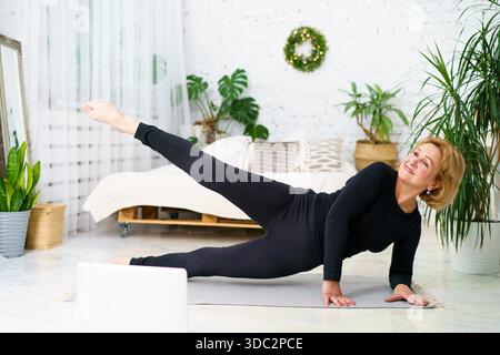Mature woman goes in for sports looking at the monitor online, home fitness for health. The concept of a healthy lifestyle in adulthood || Model released Stock Photo