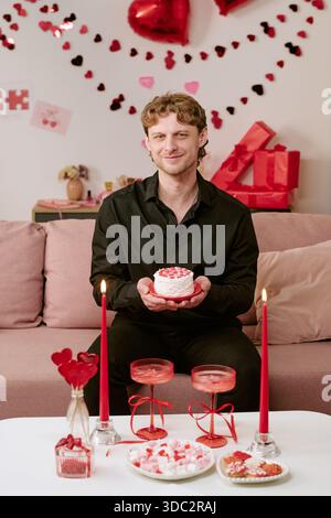 Young Man Smiling While Presenting Heart Shaped Cake on Valentines Day Stock Photo