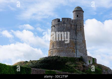 Close up view of the Vauban Tower of Saint-Vaast-la-Hougue set against a vivid blue sky with puffy white clouds, emphasizing its stone textures Stock Photo