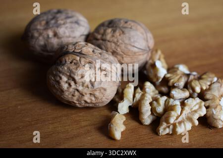 A close-up view of walnuts in their shells and peeled fresh golden walnuts, scattered on a wood surface. Healthy organic snack. Stock Photo