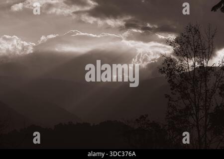 moody and dramatic monochrome sepia landscape of mountains and valleys of darjeeling with multiple sunbeams piercing heavy clouds Stock Photo