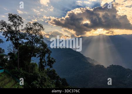 moody and dramatic landscape of mountains and valleys of darjeeling with multiple golden sunbeams piercing heavy clouds Stock Photo