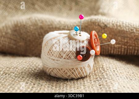 White yarn with pins and buttons on burlap cloth, closeup Stock Photo