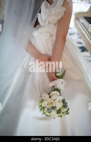 Bride holding bouquet of flowers in gorgeous white wedding dress and veil with no face showing. Stock Photo