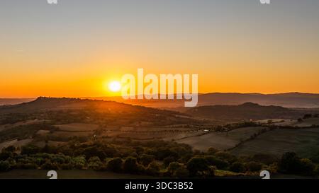 Aerial view of the sun's fiery kiss over the rolling hills, painting the landscape in hues of gold and amber, Saturnia, Tuscany, Italy. Stock Photo