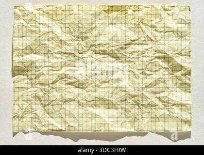 Crumpled lined yellow graph paper with grids highlighted in sunlight on white background. Stock Photo