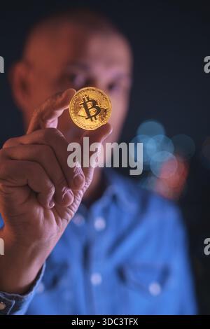Man holding a physical golden bitcoin coin with defocused background Stock Photo