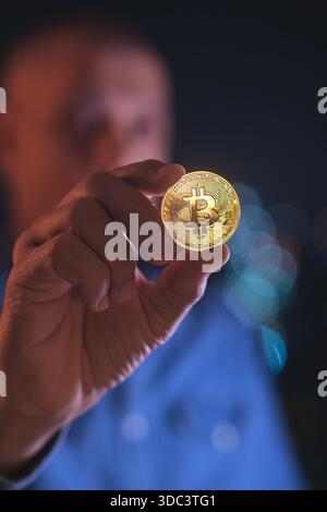 Man holding a golden bitcoin in his fingers, representing digital currency and investment Stock Photo