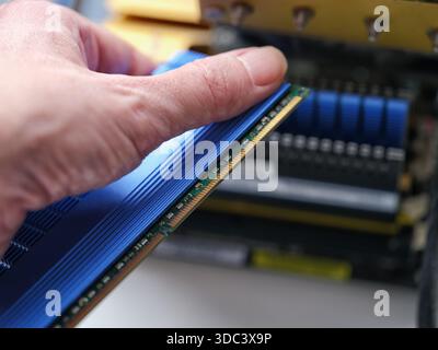 A man holding a computer RAM module with a large heat sink near a desktop motherboard. Stock Photo