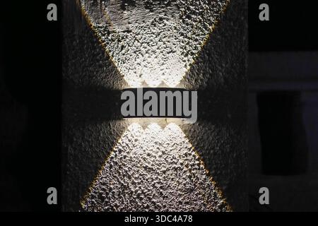Sleek wall lamp emitting dual directional light on textured plaster in nighttime setting Stock Photo