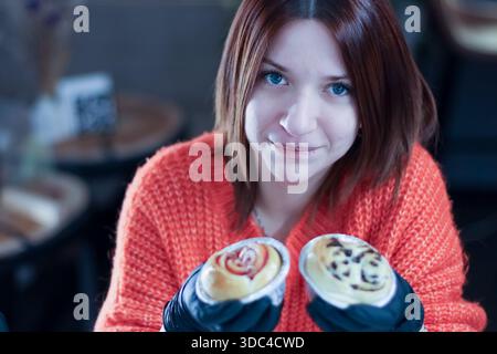 Portrait of a smiling individual in gloves presenting two themed sweet rolls in a cafe Stock Photo