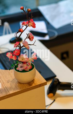 Small white pot with artificial pink flowers placed on desk beside scanner and laptop Stock Photo