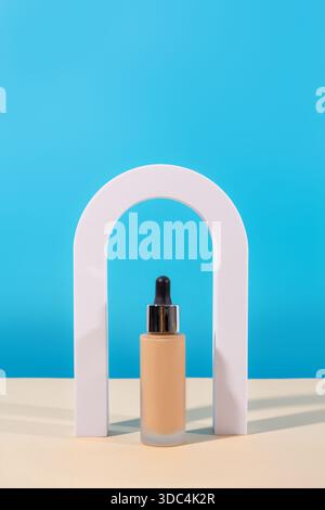 Liquid foundation cream with pipette unbranded bottle on blue background with arch. BB cream for professional make-up, eyedropper for applying to the Stock Photo