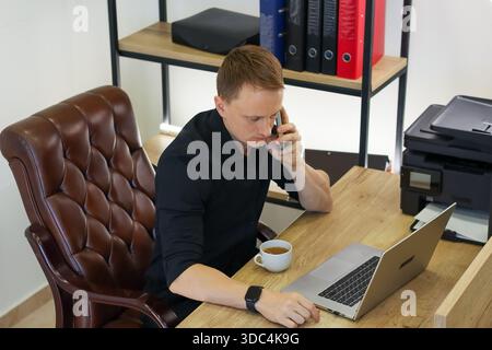 Executive engaged in call, hand on keyboard with cup and printer in background. Stock Photo