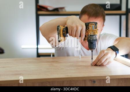 Frontal shot of person using electric drill while holding dowel in place on wooden surface during home furniture construction. Stock Photo