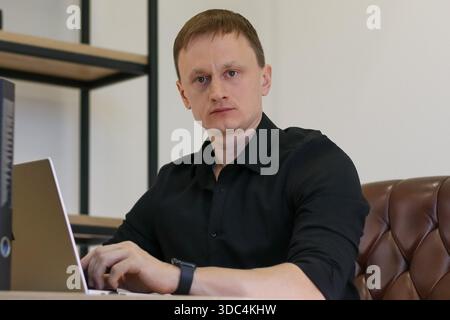 Attentive young man typing on keyboard while gazing ahead in modern office with coffee nearby Stock Photo
