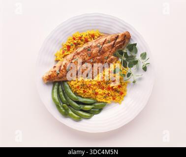 Marinated grilled catfish fillet served with saffron rice and green beans on a white plate against a white background. Studio food photograph of a hea Stock Photo