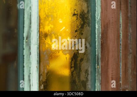 Abstract close up of worn window pane with frosted, textured glass and weathered wood frame, reflecting warm golden light and dust for a moody, vintag Stock Photo