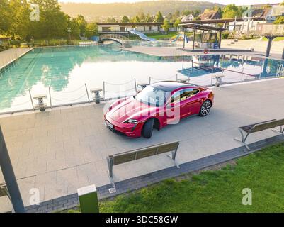 Red Porsche Taycan in parking lot next to swimming pool in relaxed landscape, Porsche Taycan, Deer Carsharing, Calw, Germany Stock Photo