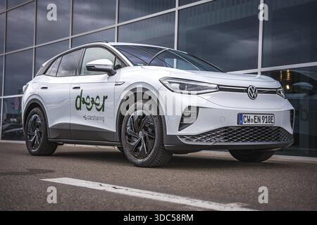 Side view of white car in front of glass facade with blue sky, VW ID4 electric car, Deer Carsharing, Calw, Germany Stock Photo