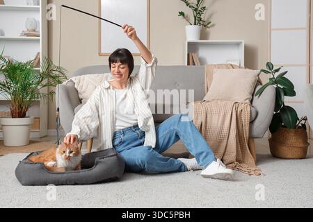 Young woman playing with cute ginger cat on floor at home Stock Photo