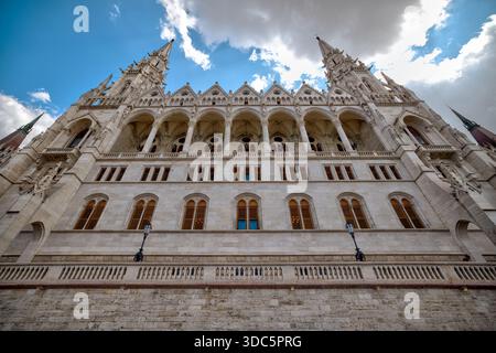 Low-angle exterior view of the Hungarian Parliament Building, showcasing Neo-Gothic architecture, spires, arches, and dramatic clouds. Stock Photo