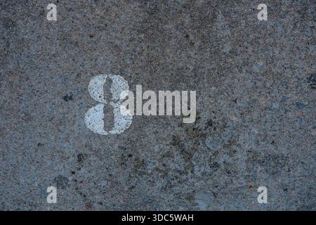 Top-down view of a white painted number 8 on rough asphalt pavement, visible aggregate texture, weathered paint, outdoor daylight, no shadows Stock Photo