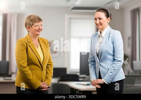 Two women sitting on a couch, both using laptops. One of the women is wearing a yellow jacket Stock Photo