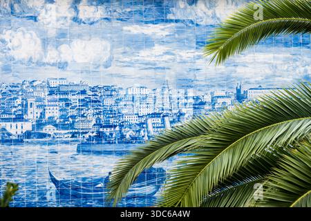 Palm leaves partially obscure a traditional azulejo tile mural showing a historic riverside city. Stock Photo
