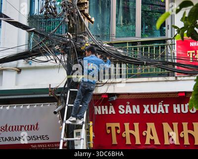 hanoi-Vietnam-August 9, 2019,A Saigontourist Cable TV technician works on an extremely tangled mass of electrical and communication wires from a ladde Stock Photo