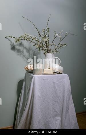 Minimal rustic breakfast setup with ceramic pitcher containing blooming cherry branches butter dish bread slice on plate ceramic cup on linen tableclo Stock Photo