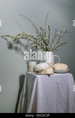 Minimal rustic breakfast setup with ceramic pitcher containing blooming cherry branches butter dish bread slice on plate ceramic cup on linen tableclo Stock Photo
