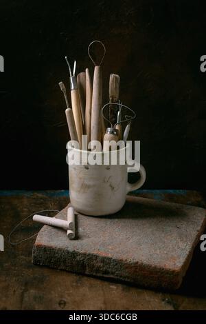 Set of clay-working tools. Old pottery tools for trimming and forming clay items in ceramic mug, wire tool, cutting string on aged wooden table with d Stock Photo