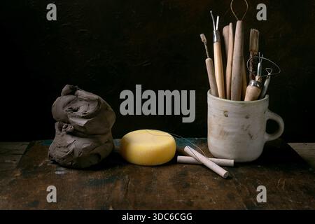 Set of clay-working tools. Old pottery tools for trimming and forming clay items in ceramic mug, wire tool, cutting string, sponge, pieces of raw clay Stock Photo