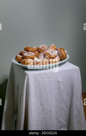 Freshly made sugar powdered donuts served on elegant blue ceramic plate. Plate placed on white tablecloth against minimalist gray background. Stock Photo